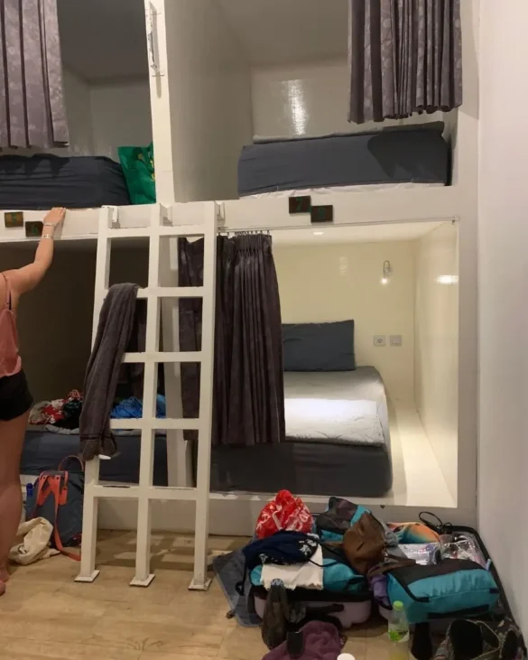 Dorm beds built into the wall in a large hostel, with a suitcase with stuff spilling out of it opened on the ground, blocking a lot of the floor