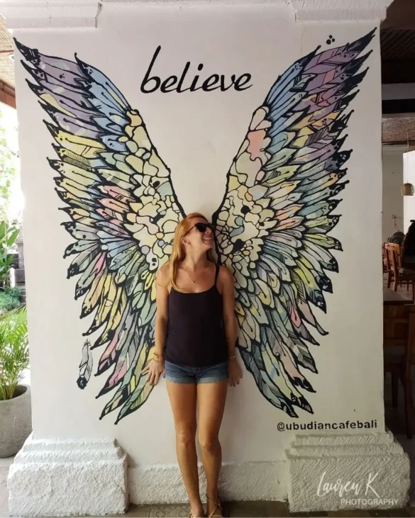 A girl standing in front of a large butterfly mural with the word "believe" above it