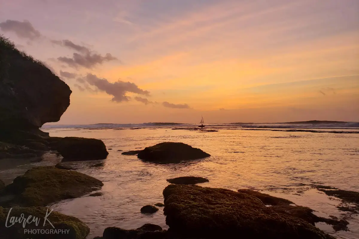 Suluban Beach Uluwatu, Bali sunset with rocks and sailboat in the background