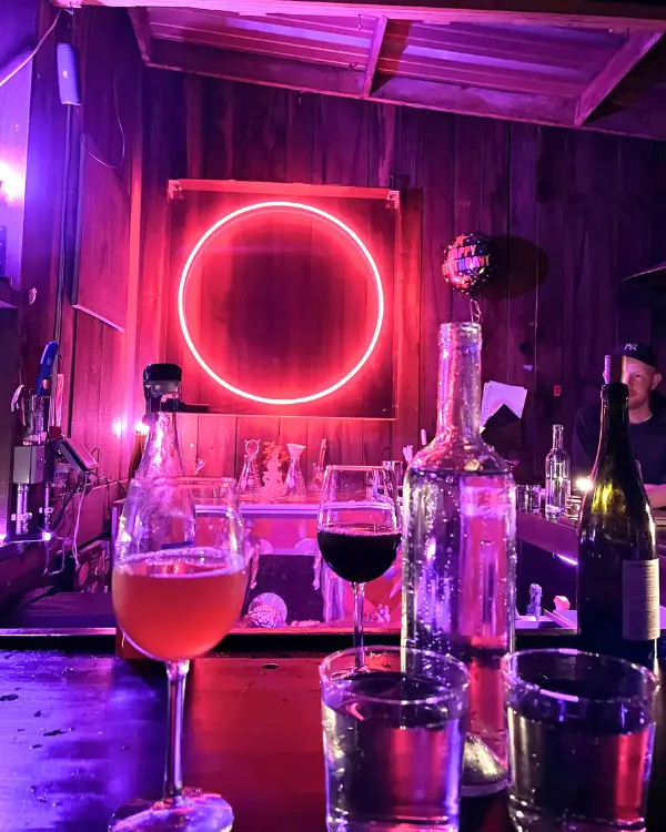 The pink moon sign and wine glasses at the bar, emitting a pink hue which is on brand for the Pink Moon Bar Asheville