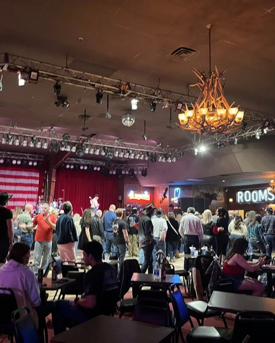 People lined up practicing a line dance in a brightly lit Coyote Joes with a big sound stage behind