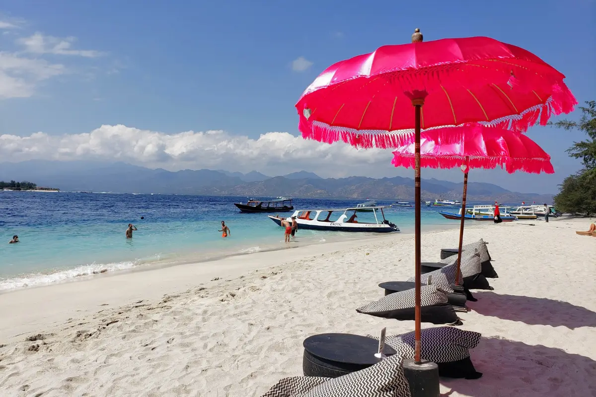Gili Trawangan beach with pink beach umbrellas. This is one of the best beaches in Bali, with mountains in the distance and calm waters.