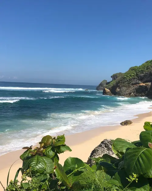 Nyang Nyang beach at high tide, from a distant view behind tropical plants