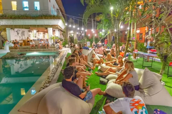 Hostel vs hotel cover image, showing a large amount of travelers socializing in the common area at Puri Garden hostel in Ubud Bali