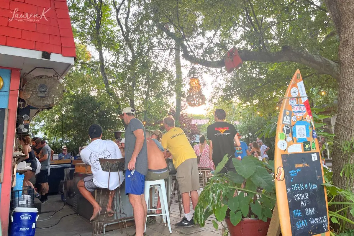Bars in Folly Beach SC cover image which shows a busy Chico Feo bar under the trees during the day time