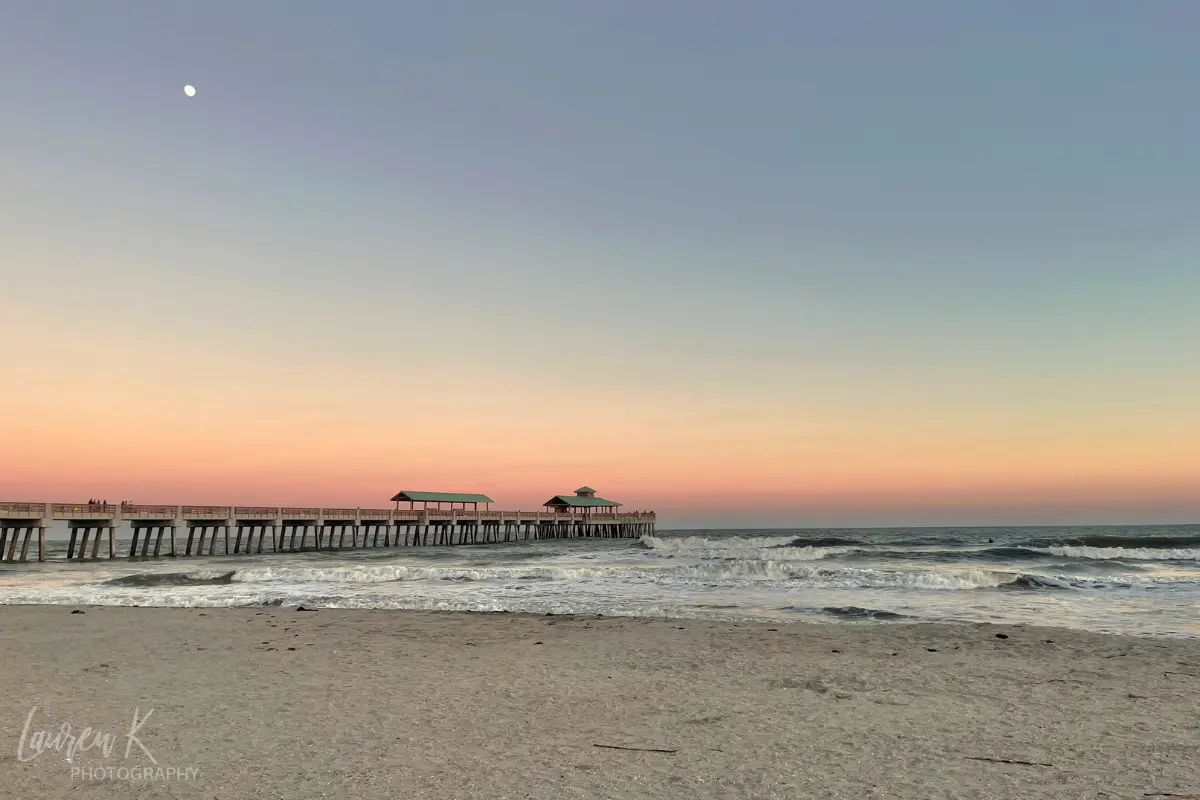 The Folly Beach pier under a sunset sky and the moon, which is one of the best Charleston SC beaches