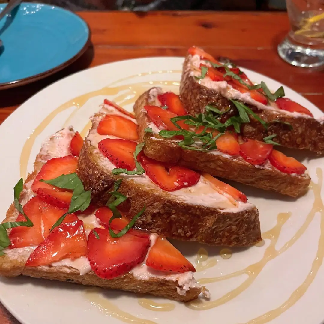 A unique toast dish with some sort of spread and fresh strawberries on top