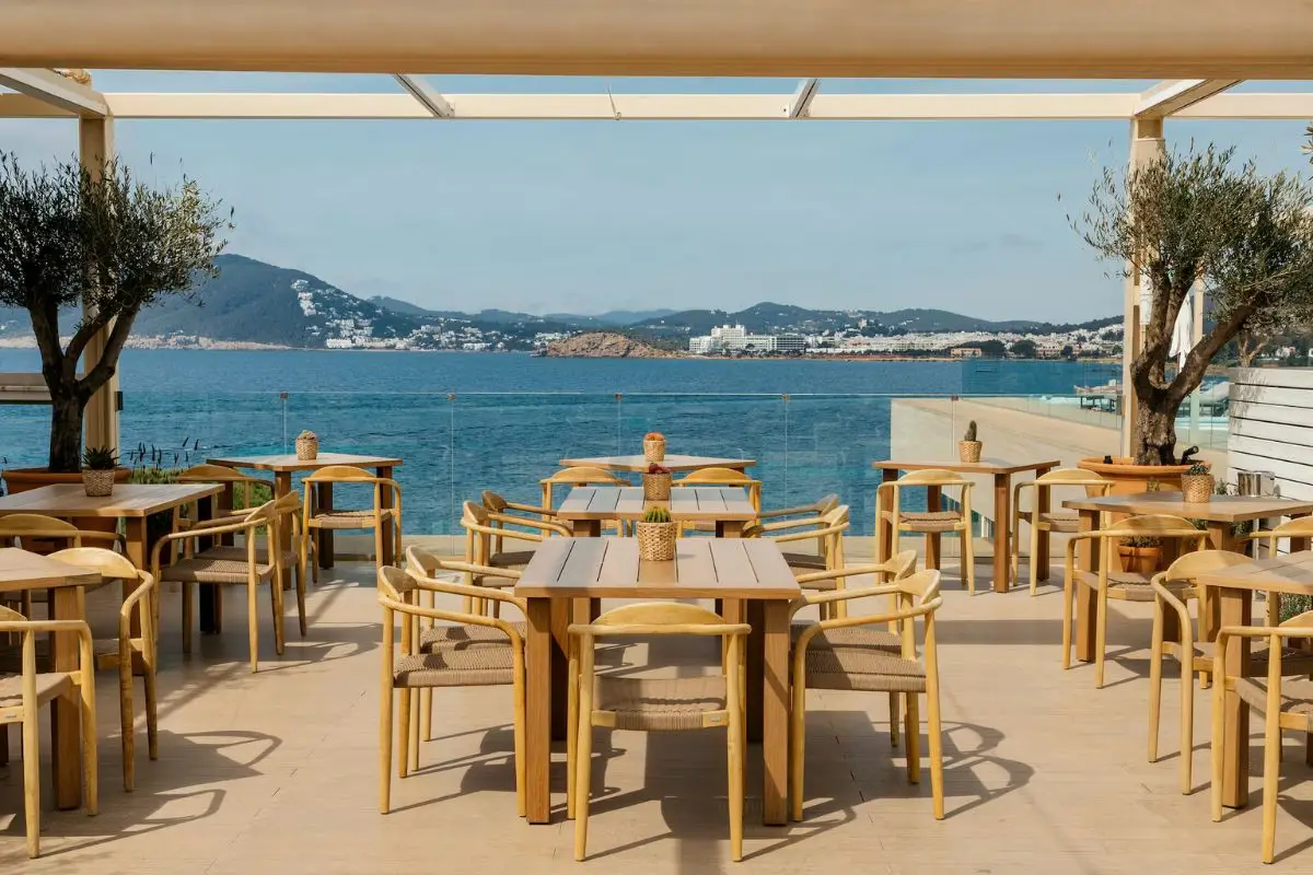 Chic chairs and tables at a modern looking bar overlooking the Mediterranean Sea and mountains on Ibiza under a cloudless sky