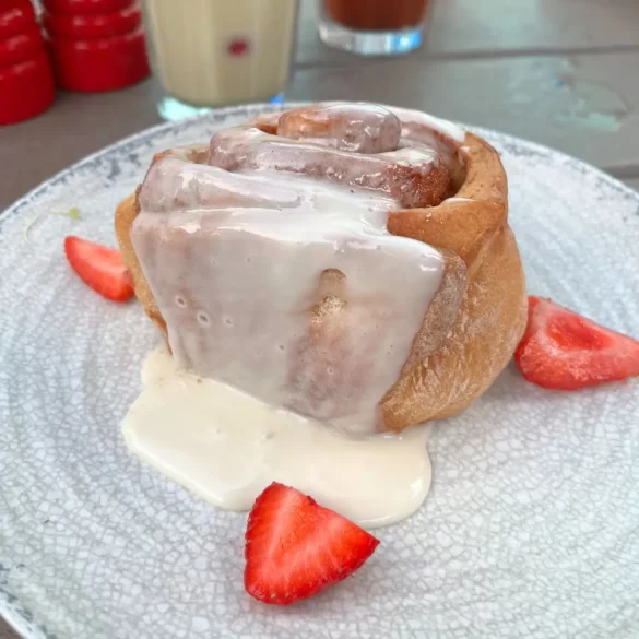 A large, gooey cinnamon roll with icing and fresh strawberries
