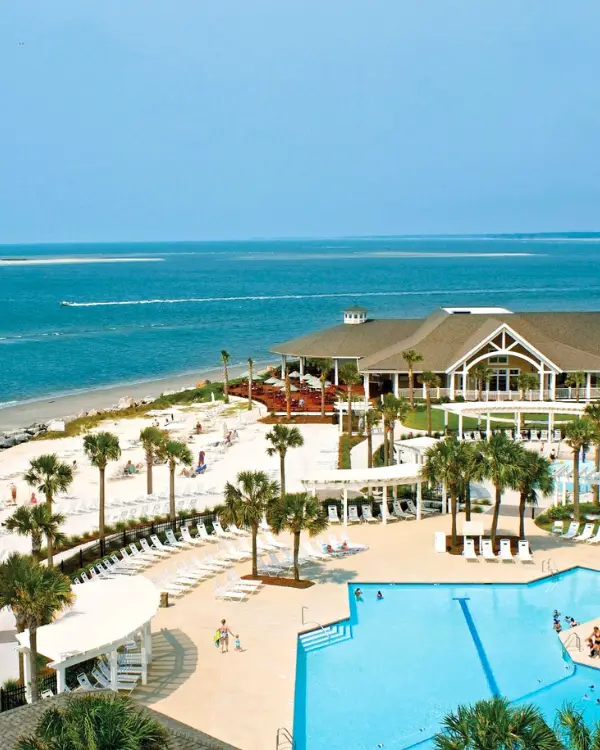 The clubhouse at the Seabrook Island Club, with the beautiful ocean behind it under sunny skies and palm trees