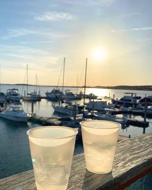 Two drinks on a pier overlooking the sunset over the water with boats on the water