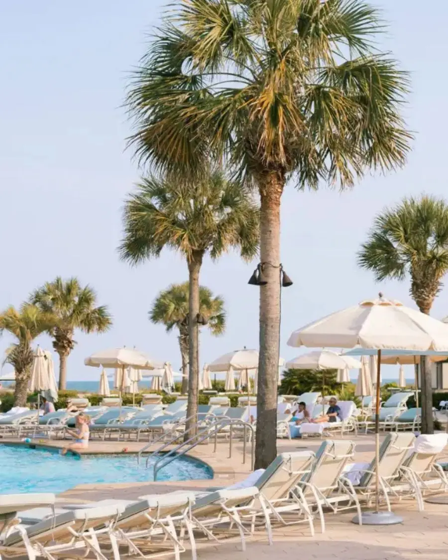 The pool deck under sunny skies at the Sanctuary resort at Kiawah Island, with a live musician playing under the shade of an umbrella