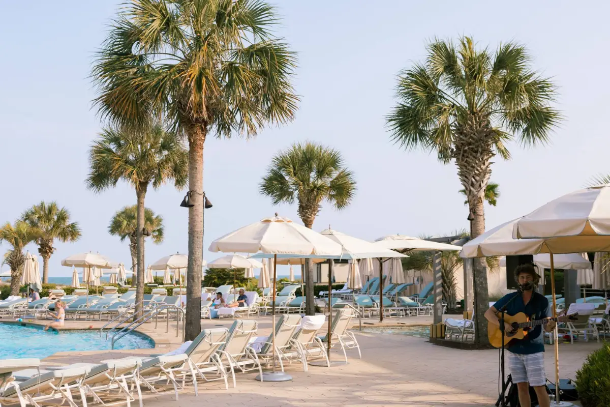 The pool deck under sunny skies at the Sanctuary resort at Kiawah Island, with a live musician playing under the shade of an umbrella