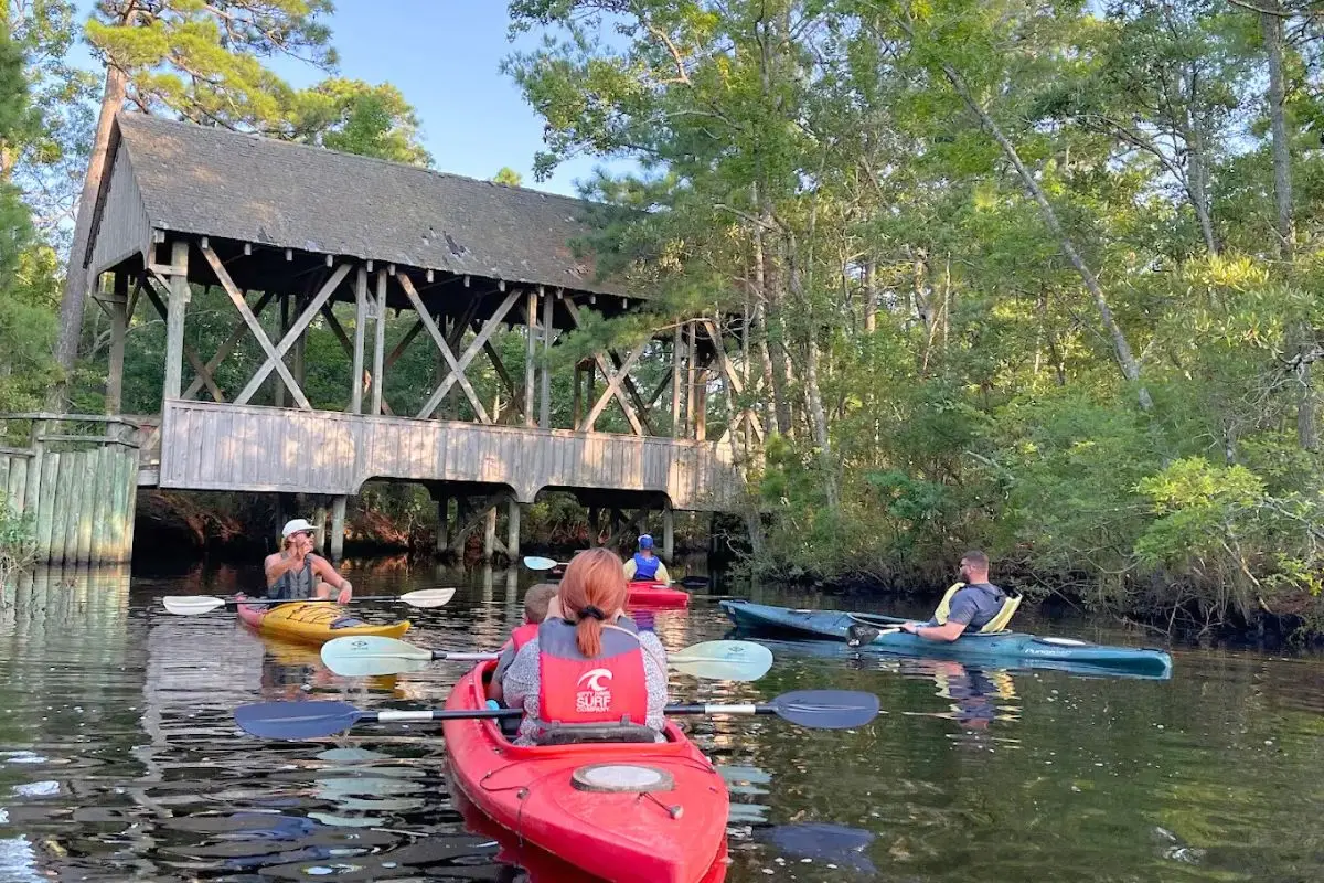 A group of people looking up at a wooden structure while kayaking on a wooded river
