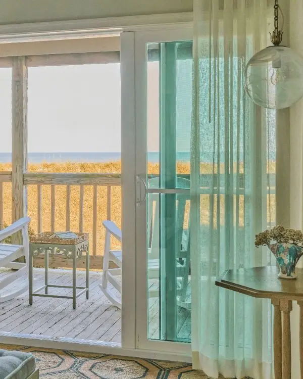 A luxury hotel room with a shaded deck and curtains, and coastal decor overlooking the ocean at the Sanderling