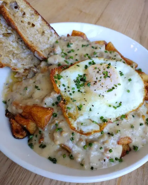 Sausage gravy topped over breakfast potatoes with a fried egg on top and bread on the side, showing that Magpie Diner is one of the best places for lunch in Harrisonburg VA