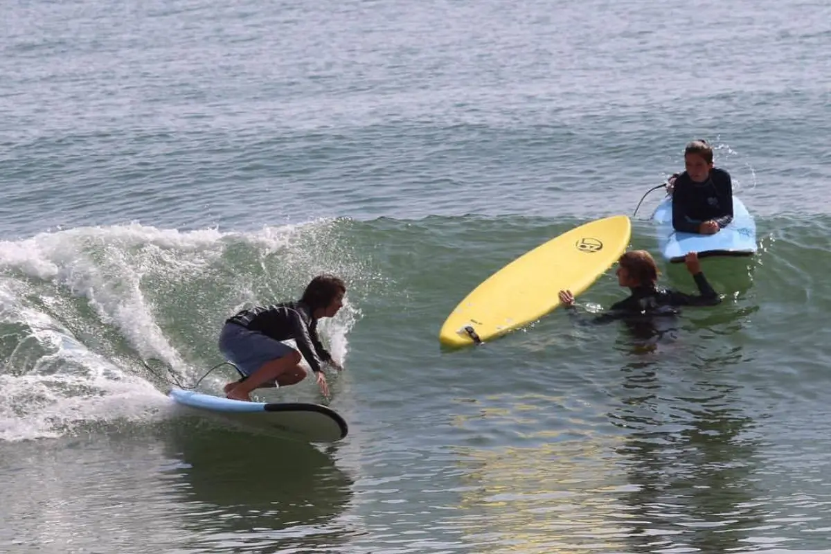 One surfer squatting down and turning on a wave while another student lays on her board and the instructor looks on