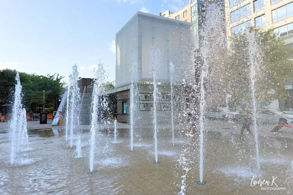 Fountains shooting up into the air at the park with the cube in the background