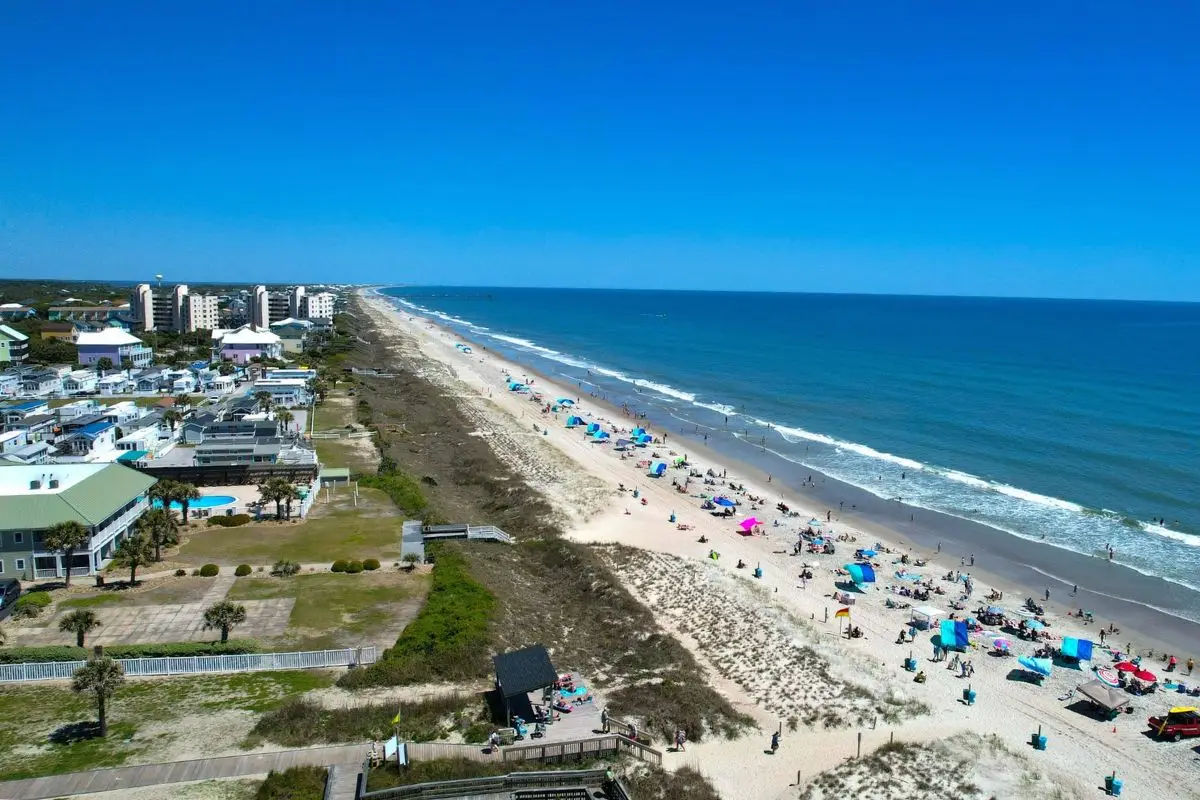 An aerial view of Emerald Isle beach, with umbrellas dotting the beach and the waves crashing on the shore with accommodations just off the beach