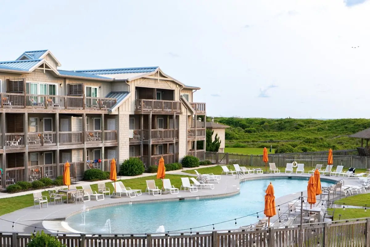 The zero entry pool with luonge chairs and umbrellas behind the dunes at the Sanderling, to show it's one of the best resorts to consider when deciding where to stay in Outer Banks