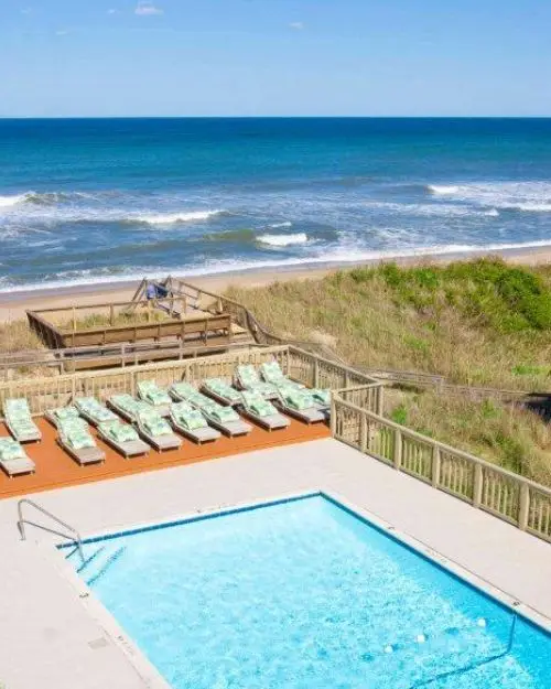 A tanning deck with lounge chairs and sparkling pool with the ocean and beach right behind, at the Surf Side hotel