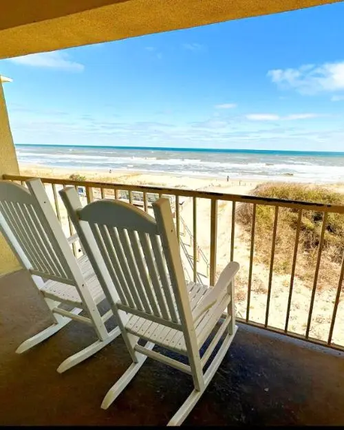 An oceanfront balcony with two rocking chairs overlooking the ocean and a blue sky at the Surf Side Hotel, to show that it's one of the best spots for where to stay in Outer Banks NC