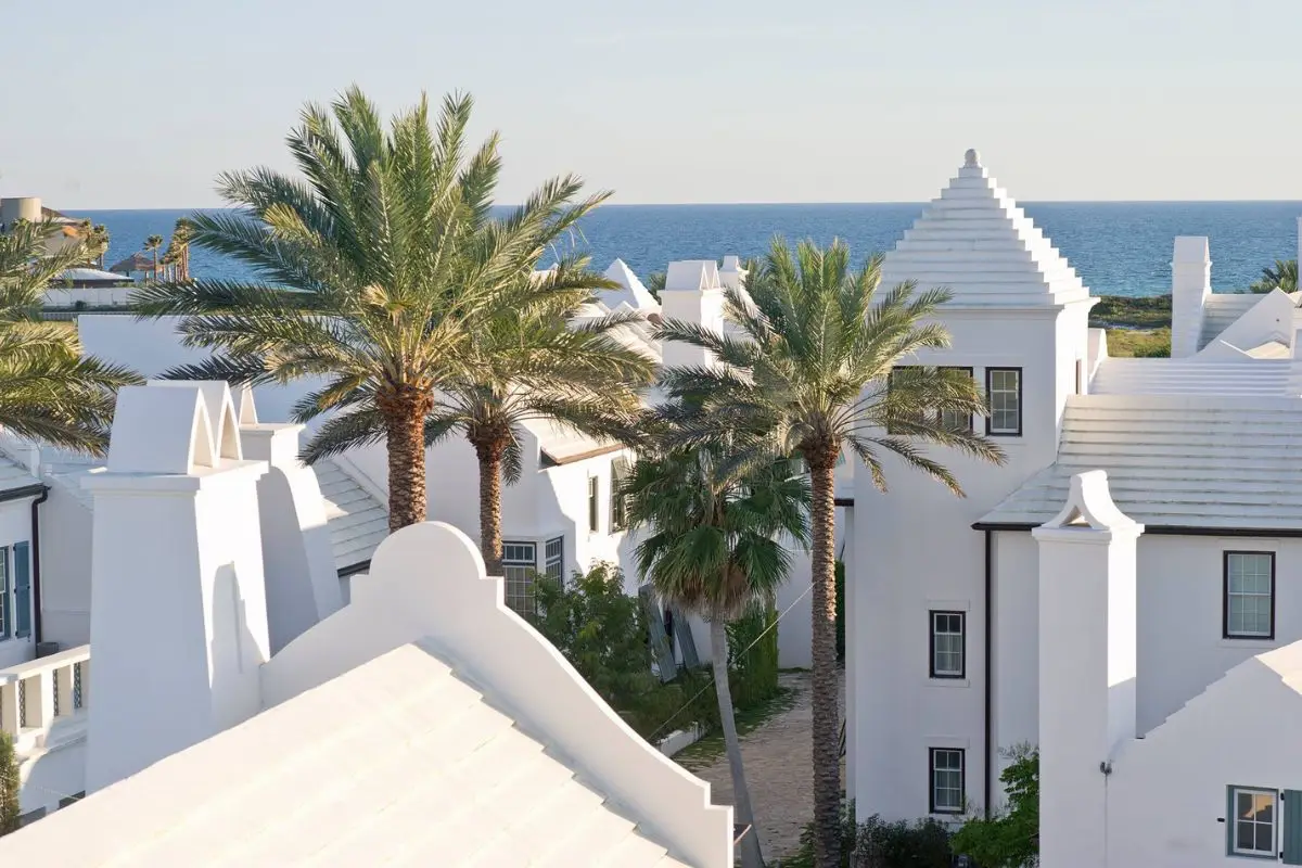 White buildings with different elements like arches and bells, with palm trees and the beautiful ocean as well