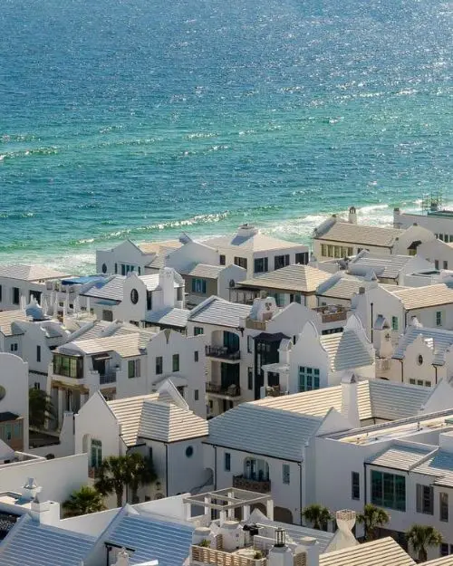 Rows of white vacation homes and buildings from above with the sparkling ocean in the background on a sunny day, which shows that Alys Beach and Rosemary Beach are two of the most beautiful beach towns in Florida. It looks like a flat Santorini