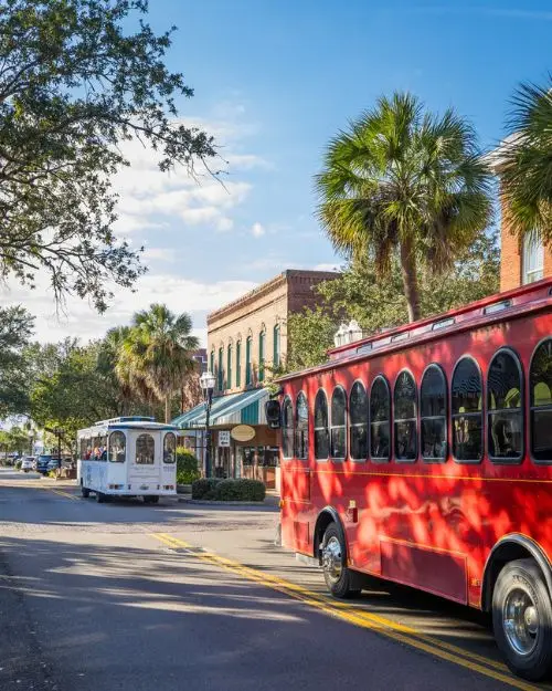 A red trolley and a white trolley on Center Street in Fernandina Beach, under the shade of palm trees