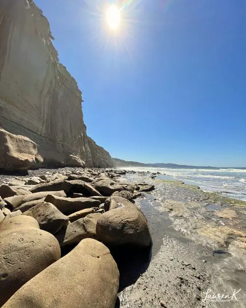 Torrey Pines State Beach, which is one of the best beaches in San Diego, during low tide with the rocks revealing themselves, the sun directly overhead and steep cliffs 