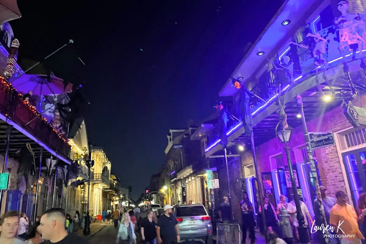 Bourbon Street in New Orleans lit up with purple, orange and green lights at night, looking extra festive for Halloween time