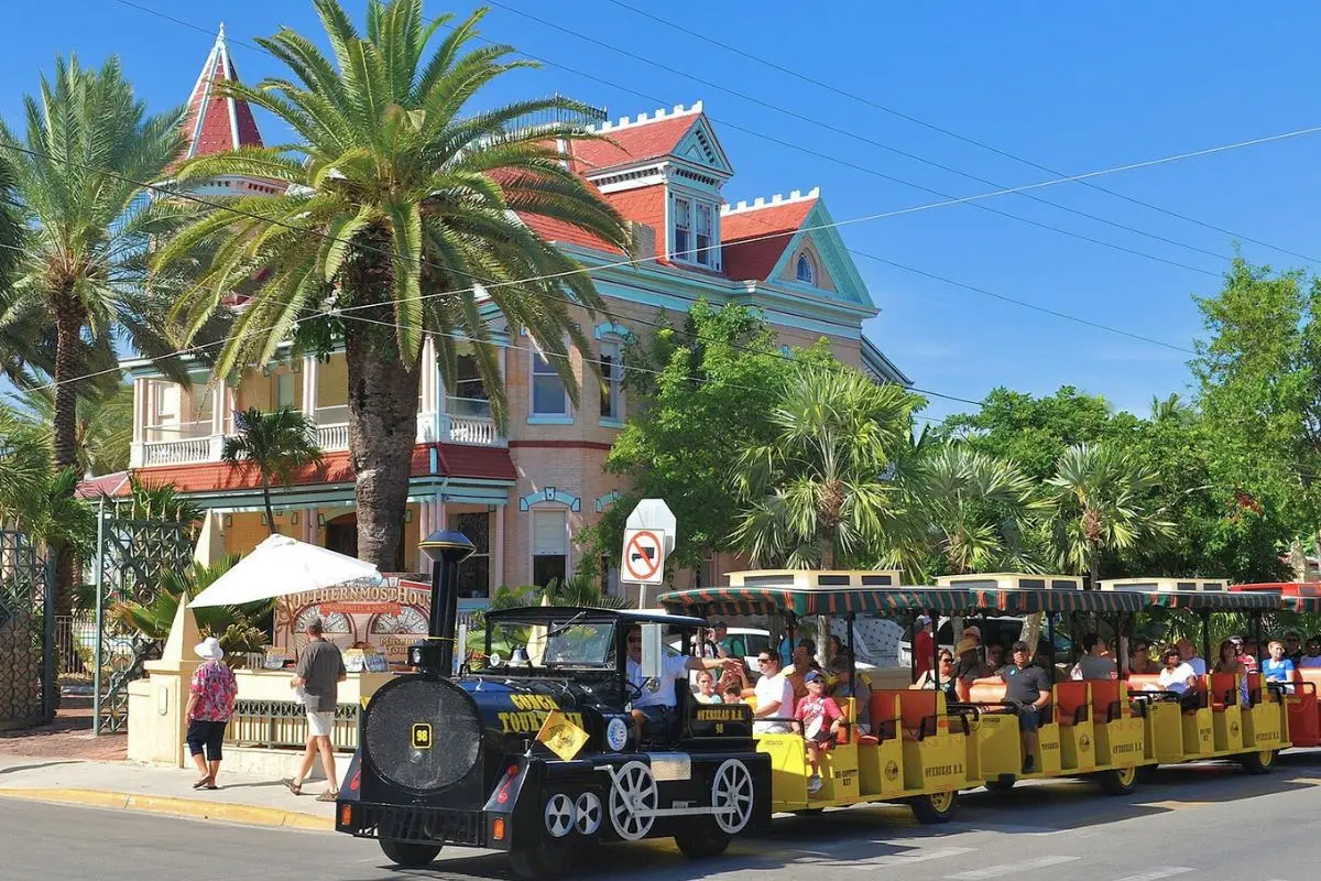 An old style train that rides around Key West and gives people a tour of the historic district, with historic buildings behind it on a sunny day