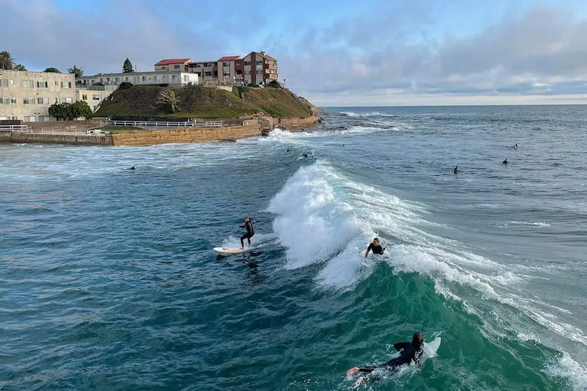 An aerial shot of the waves at Ocean Beach wi the a few surfers, one who caught the wave, at dusk 
