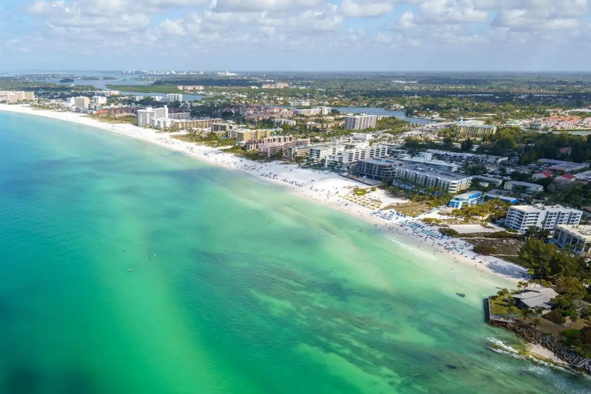 An aerial view of Siesta Keys on a sunny day showing the sandy shore and edge of town, to display one of the most beautiful and best beach towns in Florida