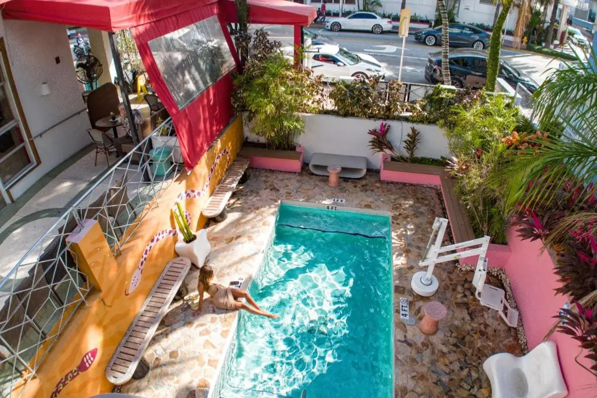 A woman dangling her legs in the small pool at Viajero Miami Hostel, with lush greenery around