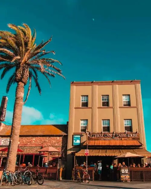 The outside of a hostel in Santa Monica along the boardwalk under a sunny sky with a palm tree closeby