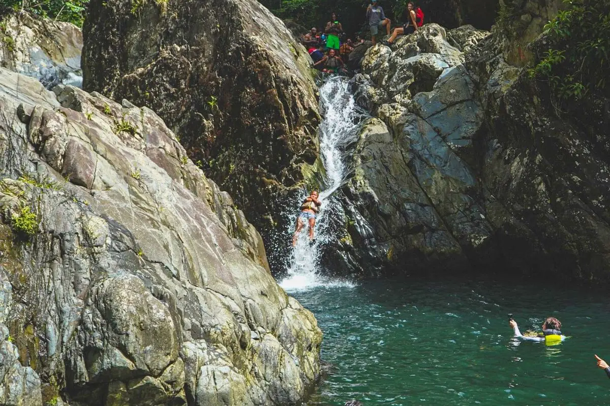 A person sliding down the natural rock slide in Puerto Rico with a group behind waiting for their turn