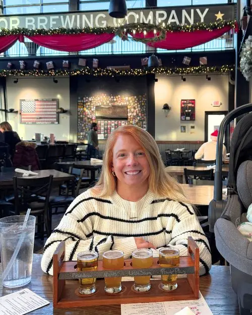 Lauren of Inspired Backpacker sitting with a beer flight at the inside room at Honor Brewing Company Loudoun with Christmas decorations overhead