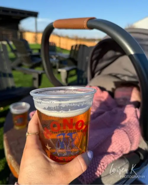 A photo of a beer at Honor Brewing Company on a sunny day with a baby carrier in the background to show it's family friendly