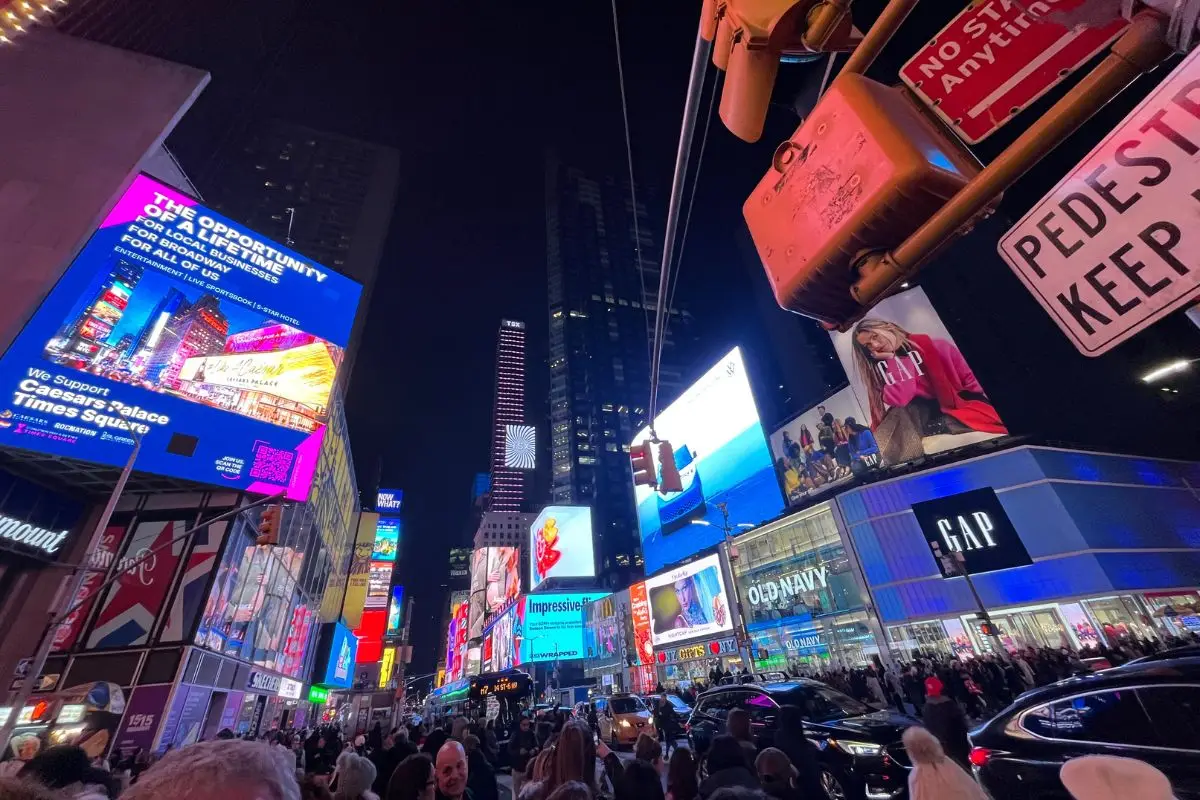 A POV shot of Times Square lit up with billboards at night, which is one of the most iconic spots in all of NYC