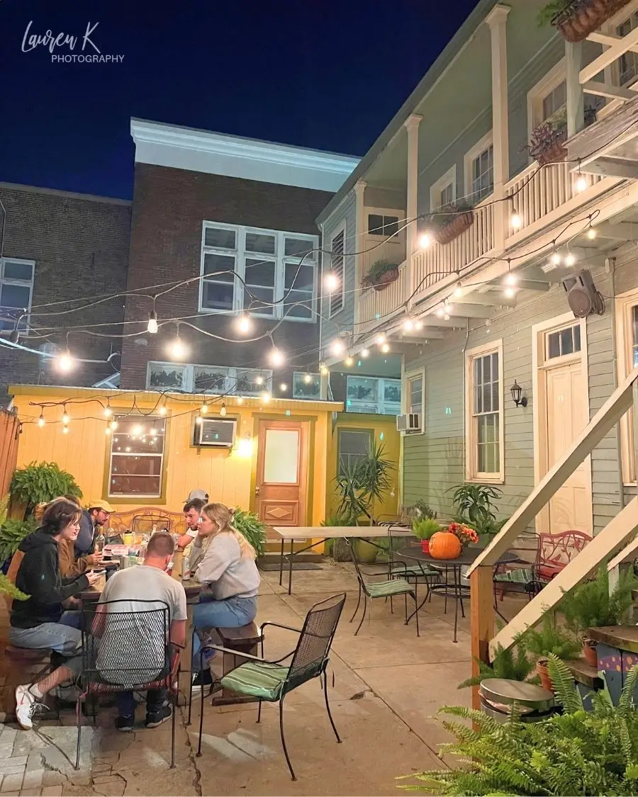 A lit up courtyard at the Auberge NOLA hostel with people sitting around a table, to show there are hostels in the US