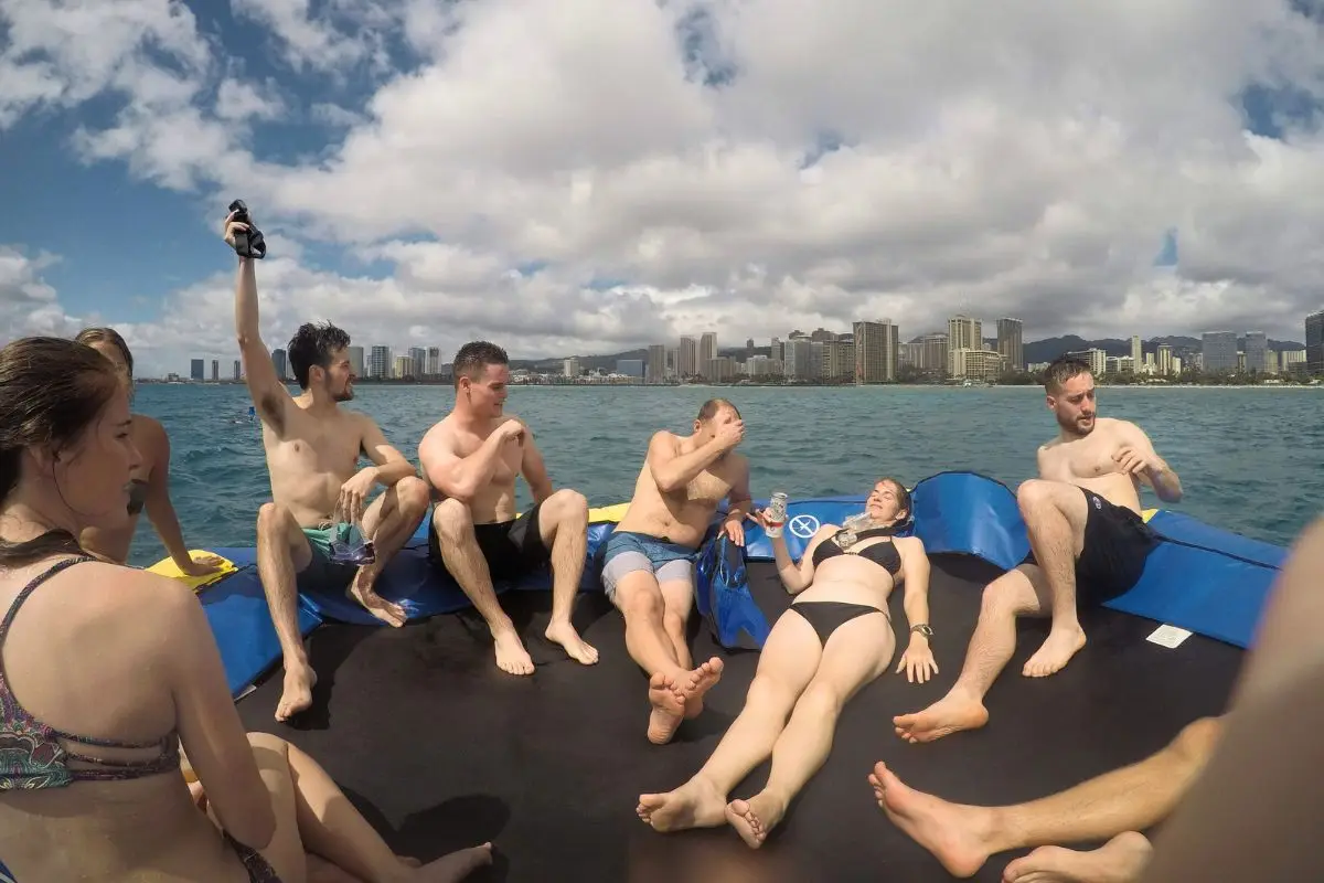 People hanging out on a trampoline on a body of water with Waikiki city in the background on a sunny day