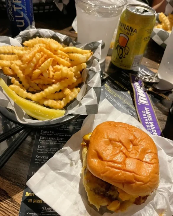 A large basket of crinkle fries and a cheesy burger in a dimly lit restaurant