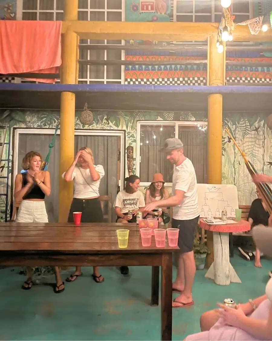 Young people laughing and enjoying themselves playing beer pong at a table at a colorful hostel courtyard