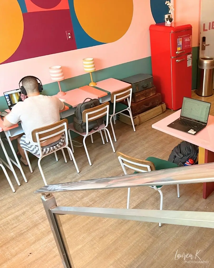 A man on a video call in a small work area and brightly colored coworking space at a hostel in Miami