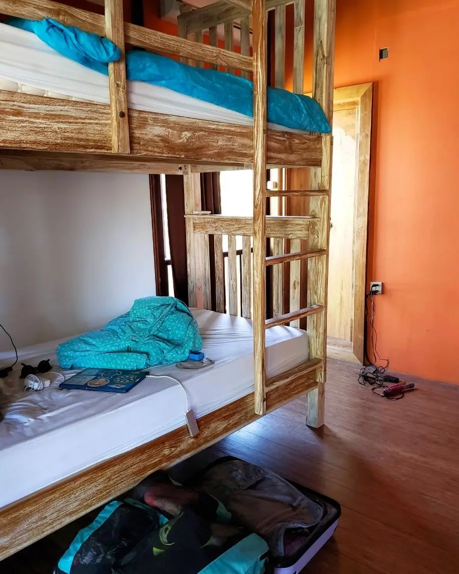 A set of wooden bunk beds with blue blankets on top and travel items scattered around the beds