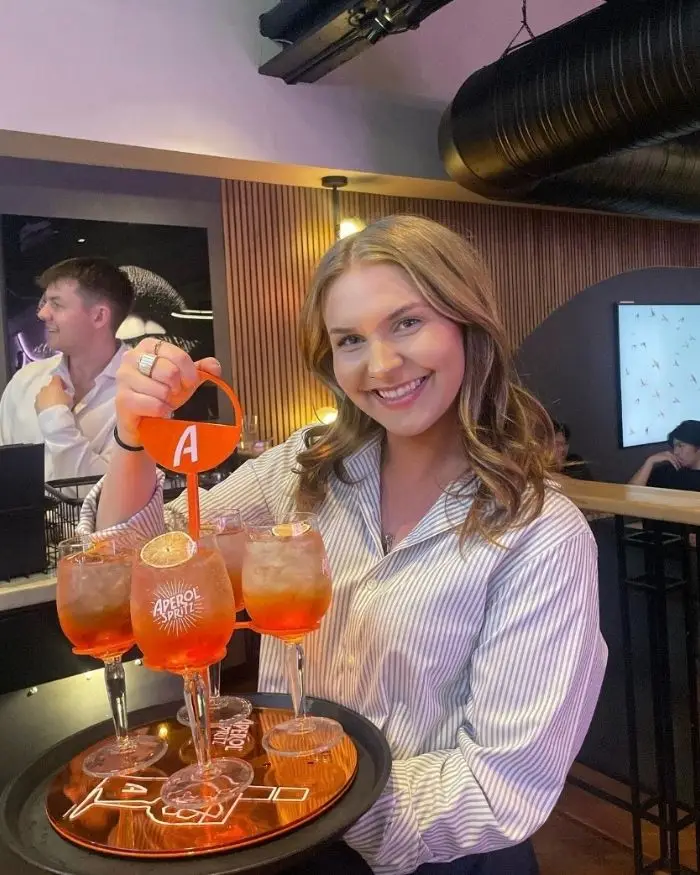 A server holding up a tower of 4 aperol spritz