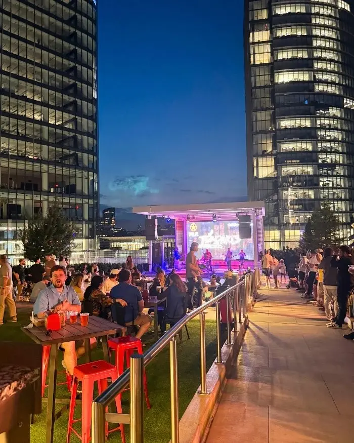 A stage lit up under the night sky and lit up high rises, with people watching the band, to show that Starr Hill Biergarten is one of the best bars in Tysons Corner VA for live music and a fun night out