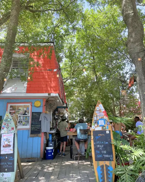 Chico Feo under the trees with people hanging out and a surf board menu at the entrance