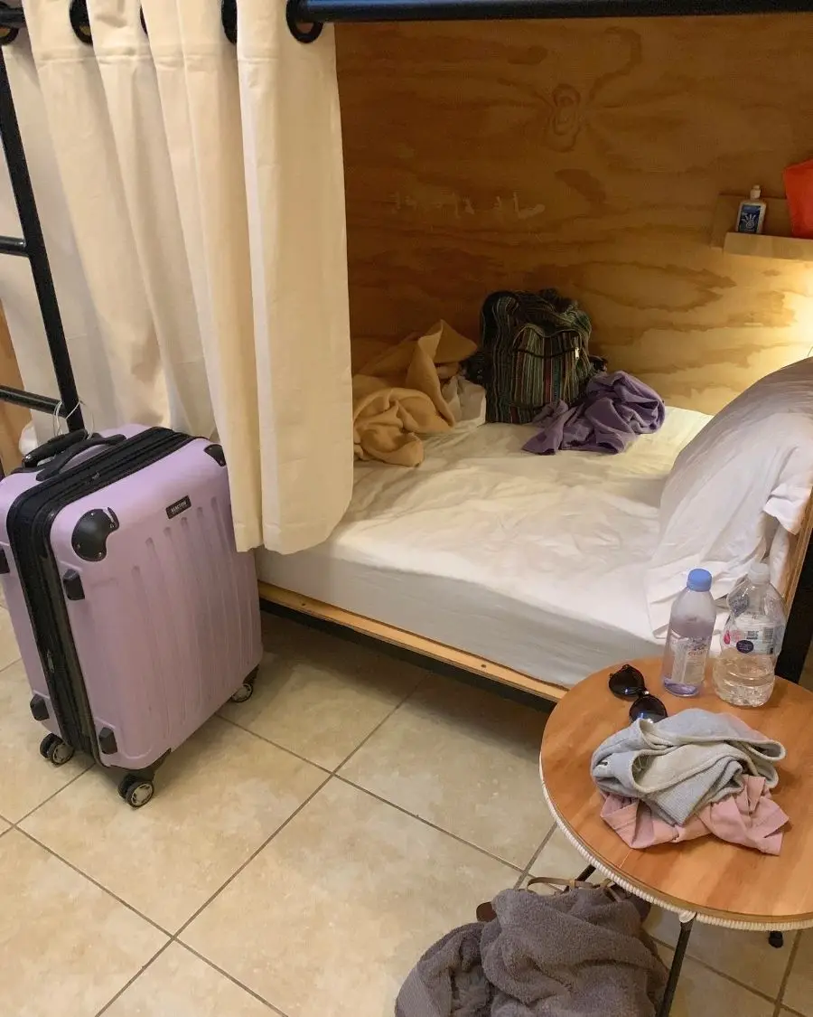 A suitcase next to a nice bottom bunk bed with a curtain